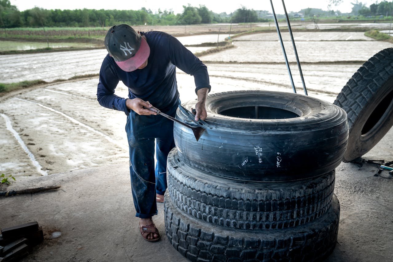 Mechanic working on large tires in an outdoor rural setting, showcasing hands-on craftsmanship.